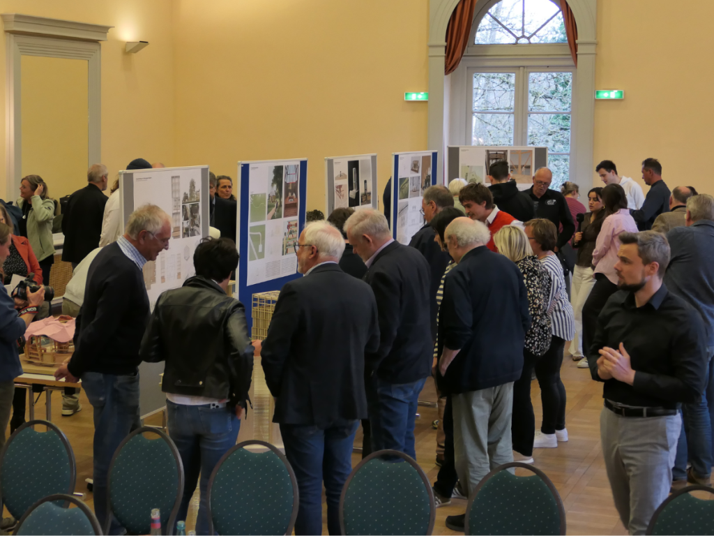 Besucherinnen und Besucher betrachten Ausstellungsmodelle und Architekturentwürfe während der Vernissage im Parksaal Bad Salzhausen.