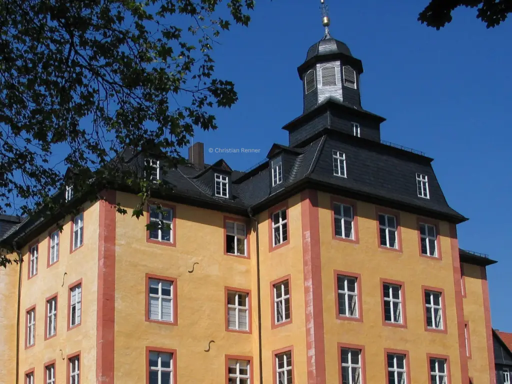 Historisches Schloss Gedern mit gelber Fassade, dunklem Schieferdach und markantem Turm vor blauem Himmel.