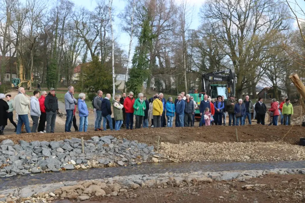 Gruppe von Menschen bei Führung an renaturiertem Bach mit Bagger im Hintergrund