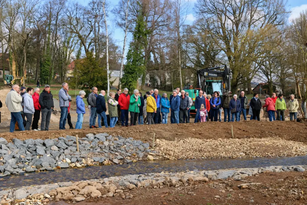 Gruppe von Menschen bei Führung an renaturiertem Bach mit Bagger im Hintergrund