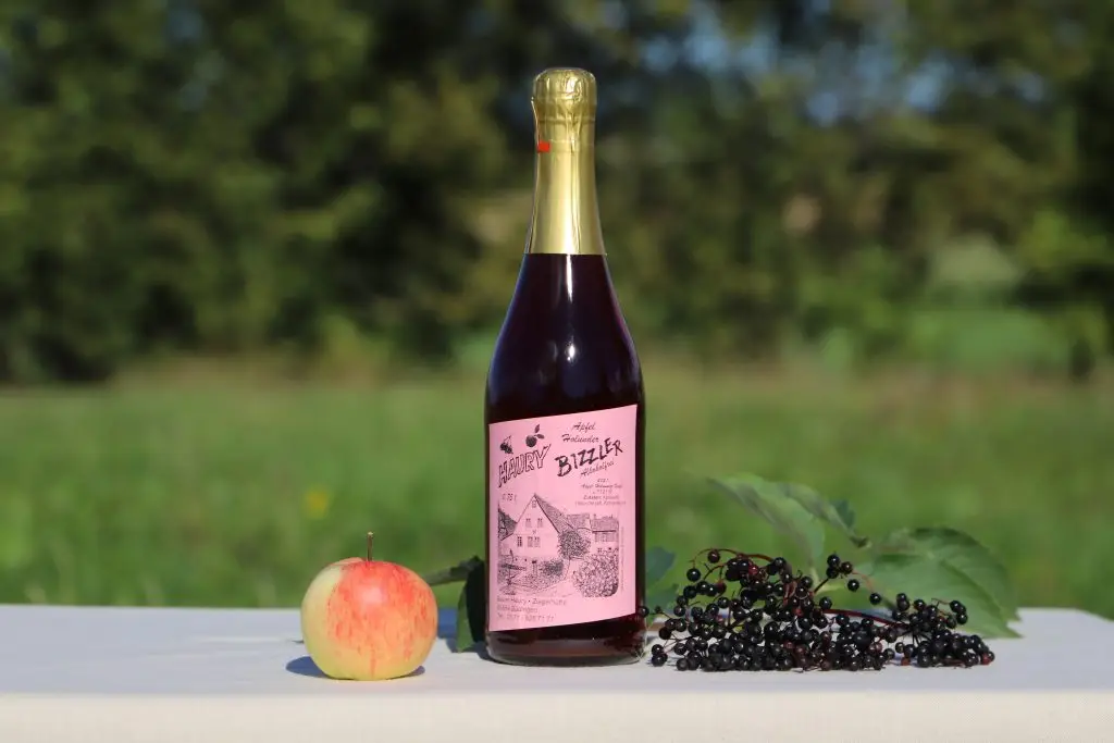 Ein Apfel und Beeren sind neben einer Flasche mit Aufdruck "Bizzler" vor grünem Hintergrund