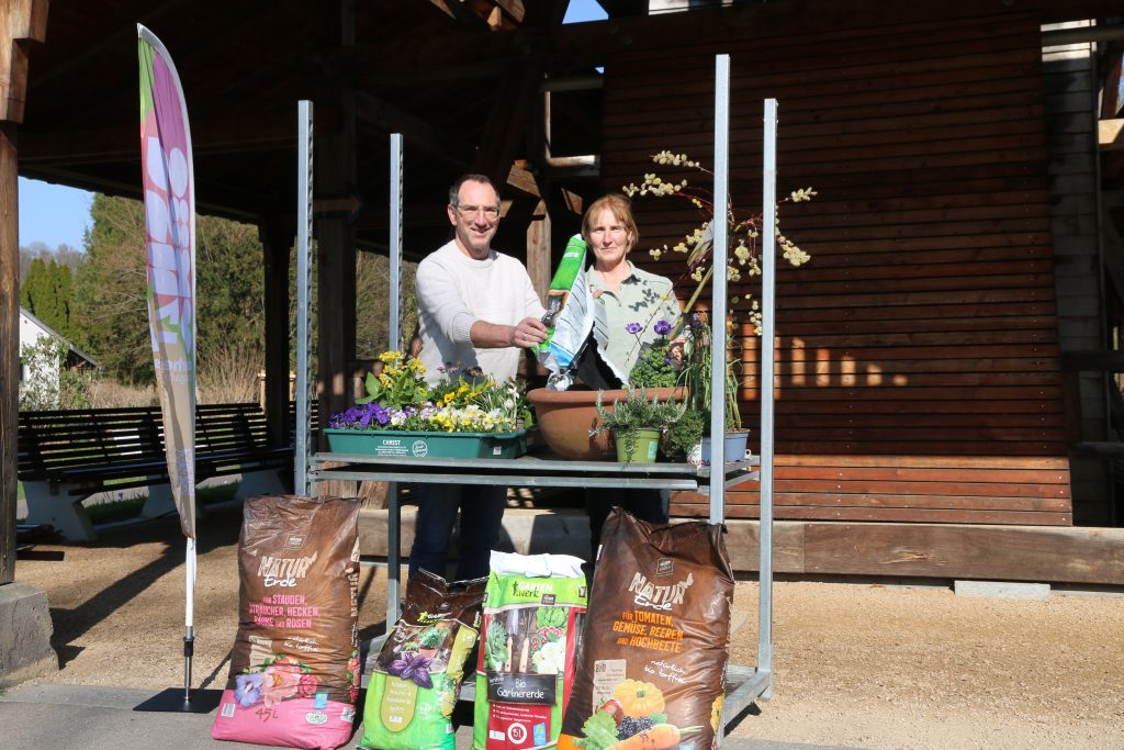 Zwei Personen präsentieren Blumen und torffreie Erde an einem Gartentisch