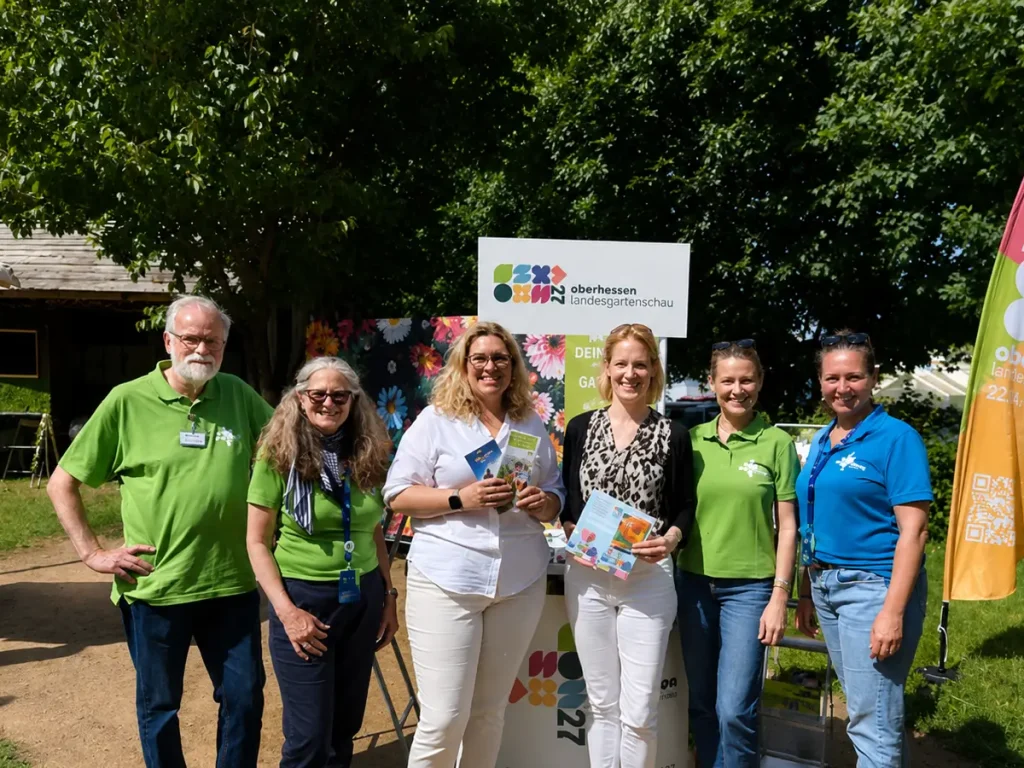 Gruppenfoto mit Gästen und Teammitgliedern an einem Informationsstand