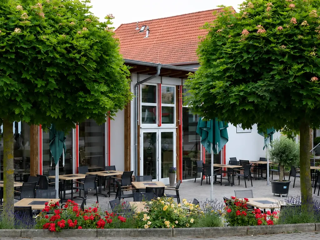 Außenansicht des Johanniter-Hotels in Butzbach mit Terrasse, blühenden Beeten und schattenspendenden Bäumen.