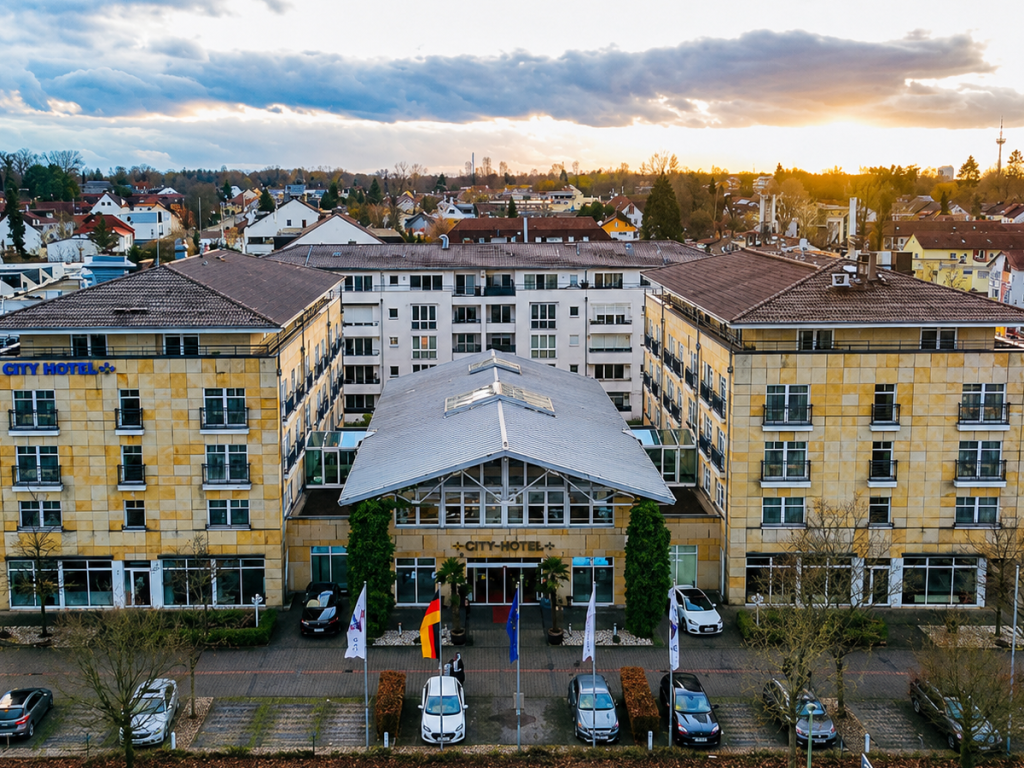 City Hotel Bad Vilbel mit markanter Eingangsarchitektur und Vorfahrt, aufgenommen aus der Vogelperspektive bei Abendstimmung.