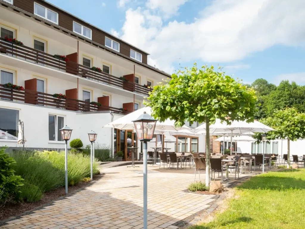 Sonnenterrasse des Hotels Sonnenberg mit Sitzplätzen im Freien, schattenspendenden Bäumen und Blick auf die Hotelanlage