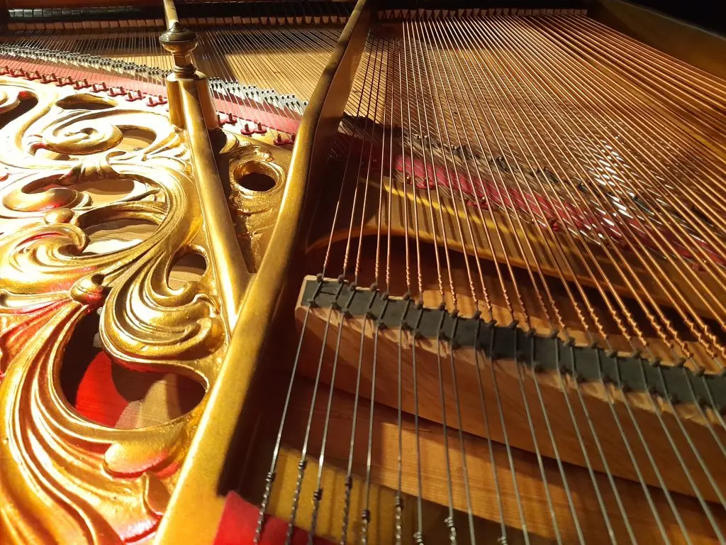 Detailaufnahme des Innenraums eines Flügels mit Saiten, Holzrahmen und goldfarbenen Verzierungen.