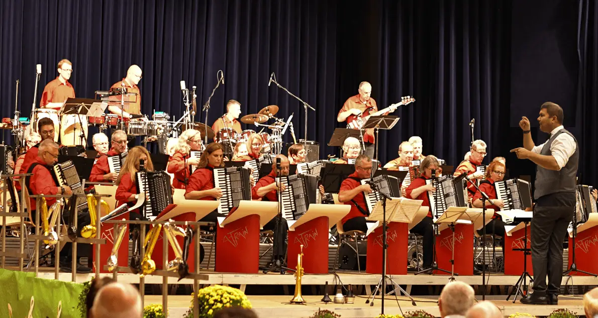 Die Landes-Akkordeon-Bigband Hessen „A-Train“ spielt auf einer Bühne unter der Leitung ihres Dirigenten; im Vordergrund sitzen die Akkordeonistinnen und Akkordeonisten, dahinter Rhythmusgruppe und Schlagzeug.