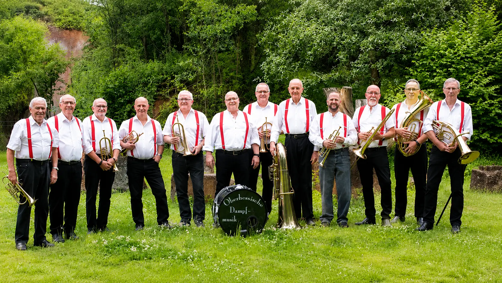 Die Oberhessische Dampfmusik posiert mit Blechblasinstrumenten auf einer Wiese.