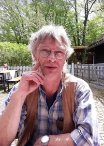 Martin Schindel sitzt an einem Tisch im Freien und blickt in die Kamera.