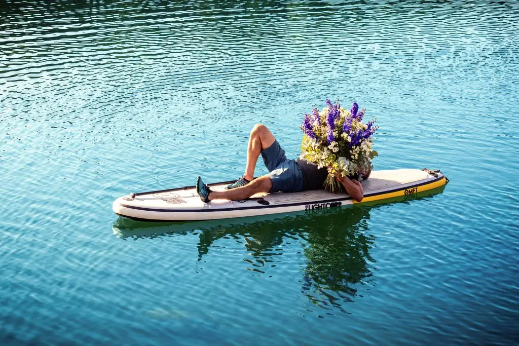 Person auf einem mit Blumen geschmückten Board auf ruhigem Wasser