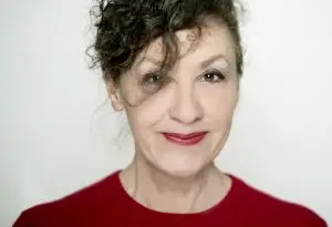 Porträt einer lächelnden Autorin mit dunklen Locken und rotem Oberteil.