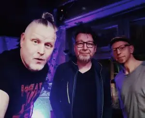 Die drei Mitglieder der Band Green Rock posieren unter violett-blauer Beleuchtung für die Kamera.