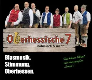 Die Oberhessische 7 posiert in traditioneller Tracht vor ihrem Bandlogo.