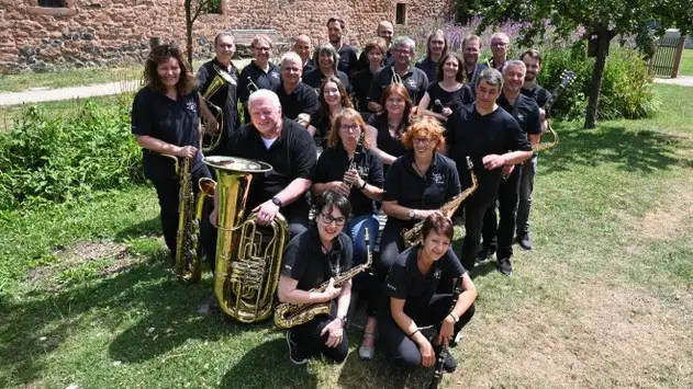 Eine große Band posiert mit Blasinstrumenten gemeinsam im Freien.