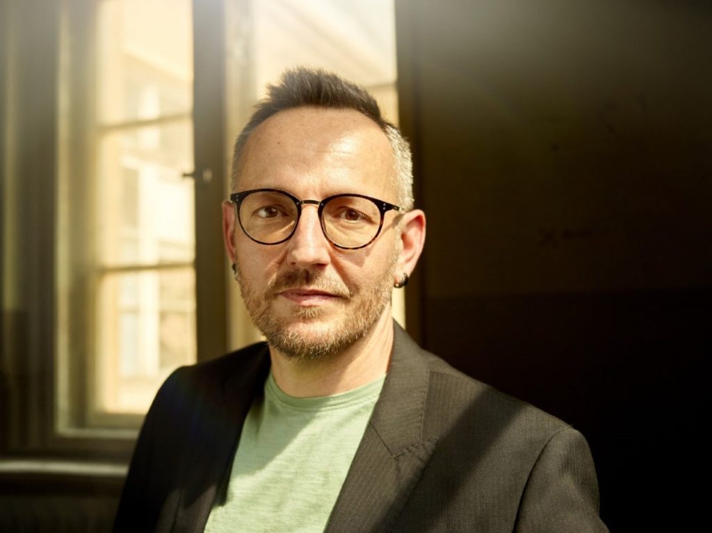Porträt des Autors Daniel Holbe mit Brille und dunklem Sakko in einem Innenraum.
