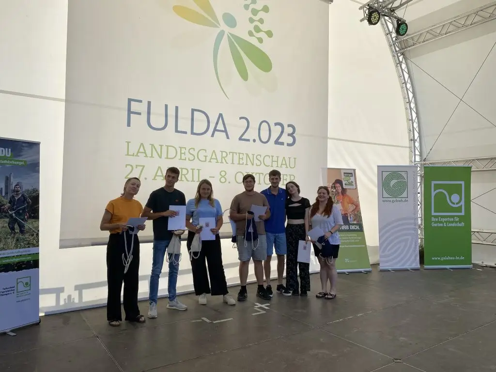 Sieben junge Erwachsene stehen mit Urkunden und Stoffbeuteln auf einer Bühne der Landesgartenschau Fulda 2023.