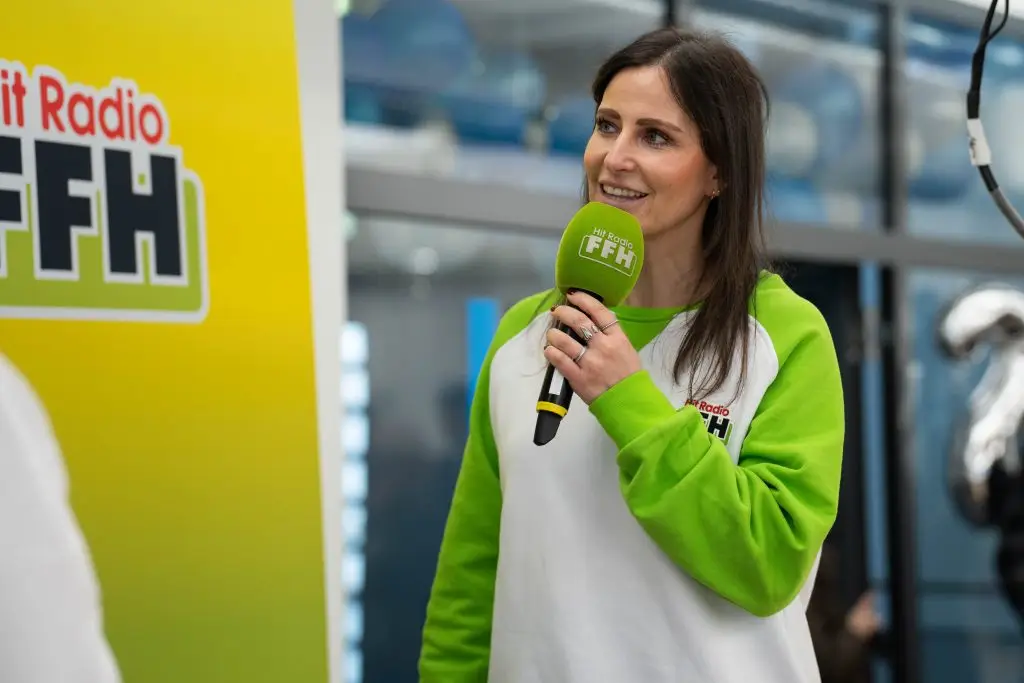 Radiomoderatorin Julia Nestle spricht mit einem grünen Hit-Radio-FFH-Mikrofon bei einer Veranstaltung.