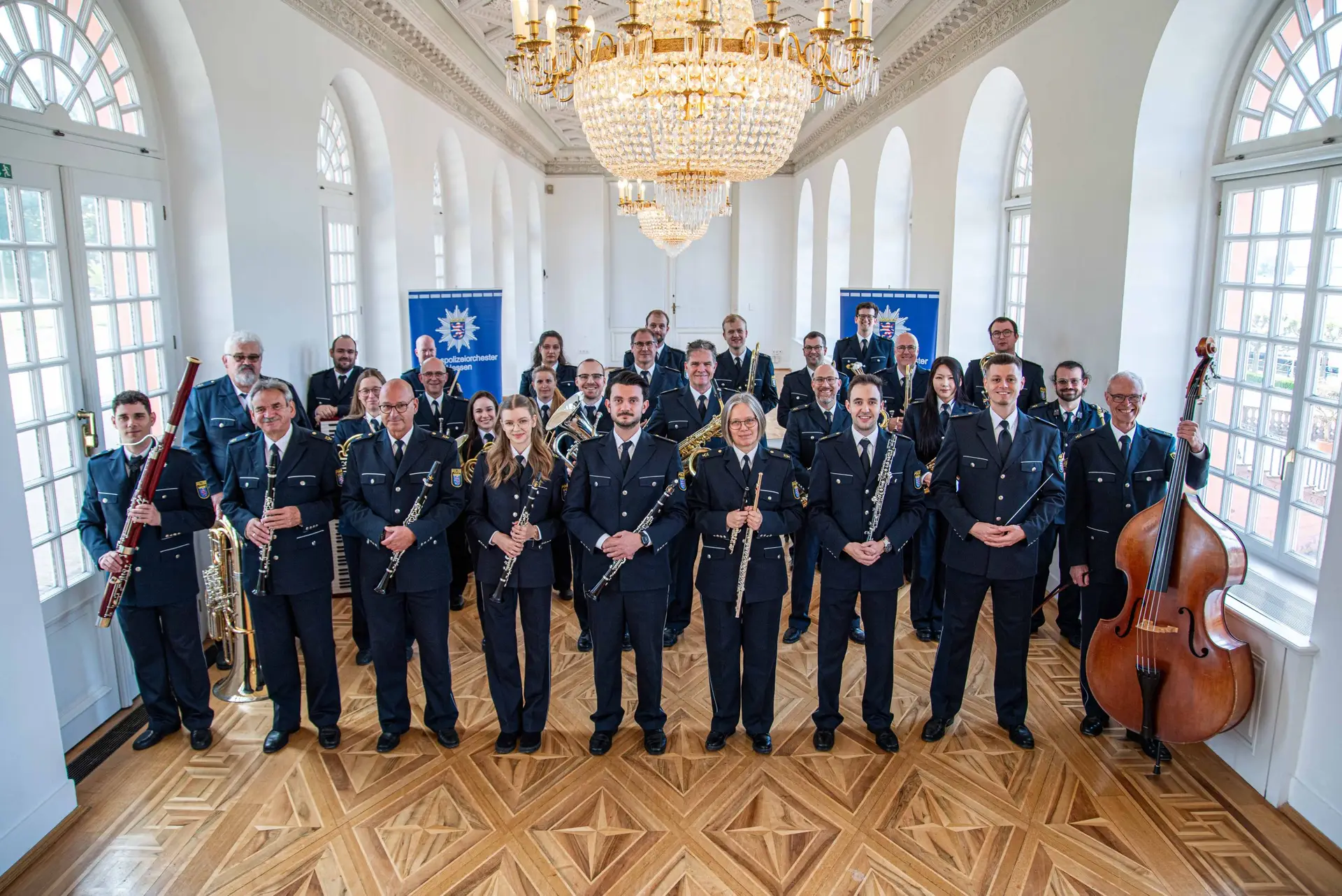 Das Landespolizeiorchester posiert in Uniformen mit verschiedenen Blas- und Streichinstrumenten in einem festlichen Saal.