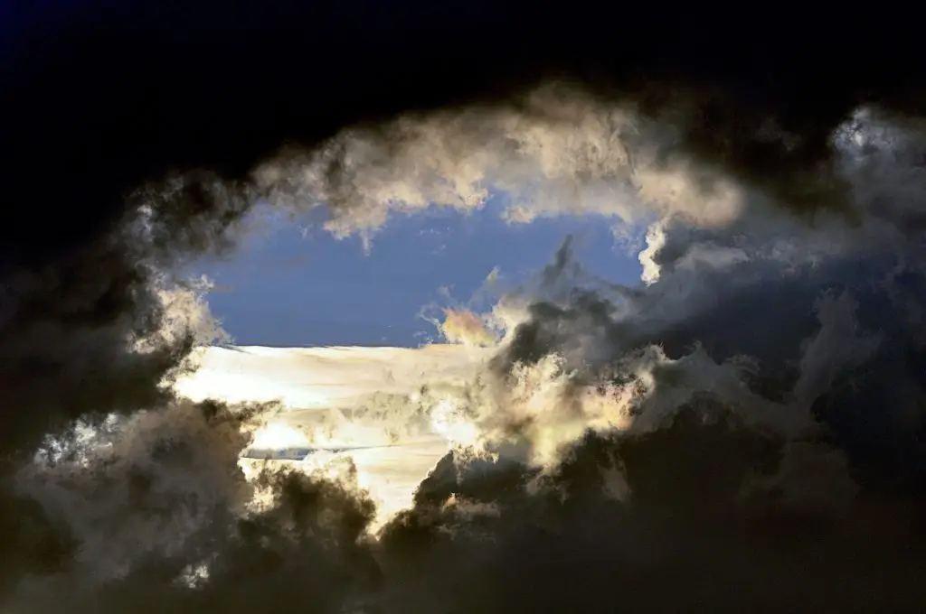Dunkle Wolken öffnen den Blick auf einen hell erleuchteten blauen Himmelsausschnitt.