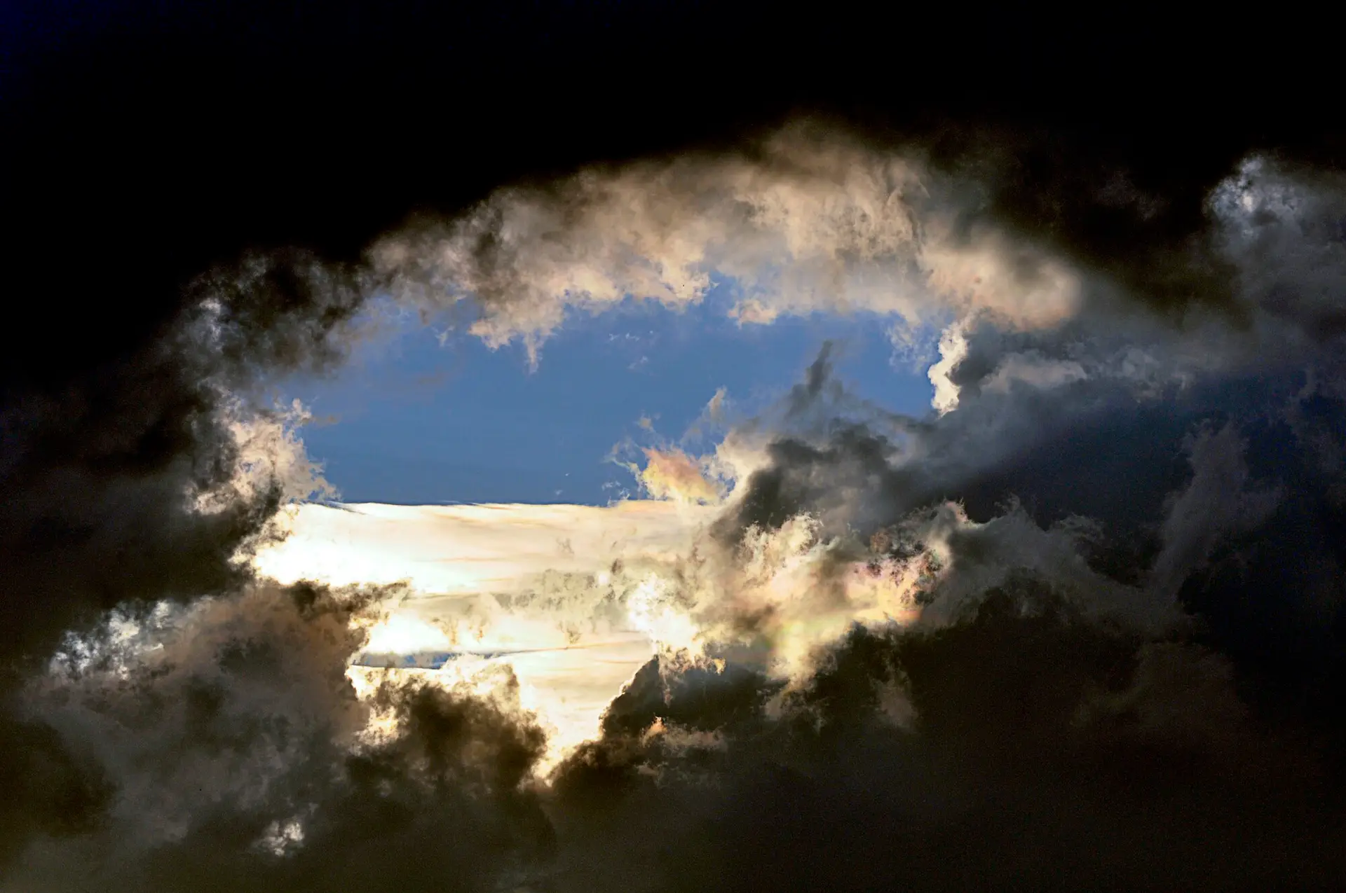 Dunkle Wolken öffnen den Blick auf einen hell erleuchteten blauen Himmelsausschnitt.
