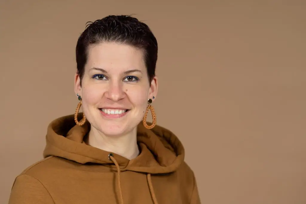 Porträt von Anne Schneider mit kurzem dunklem Haar und braunem Kapuzenpullover.