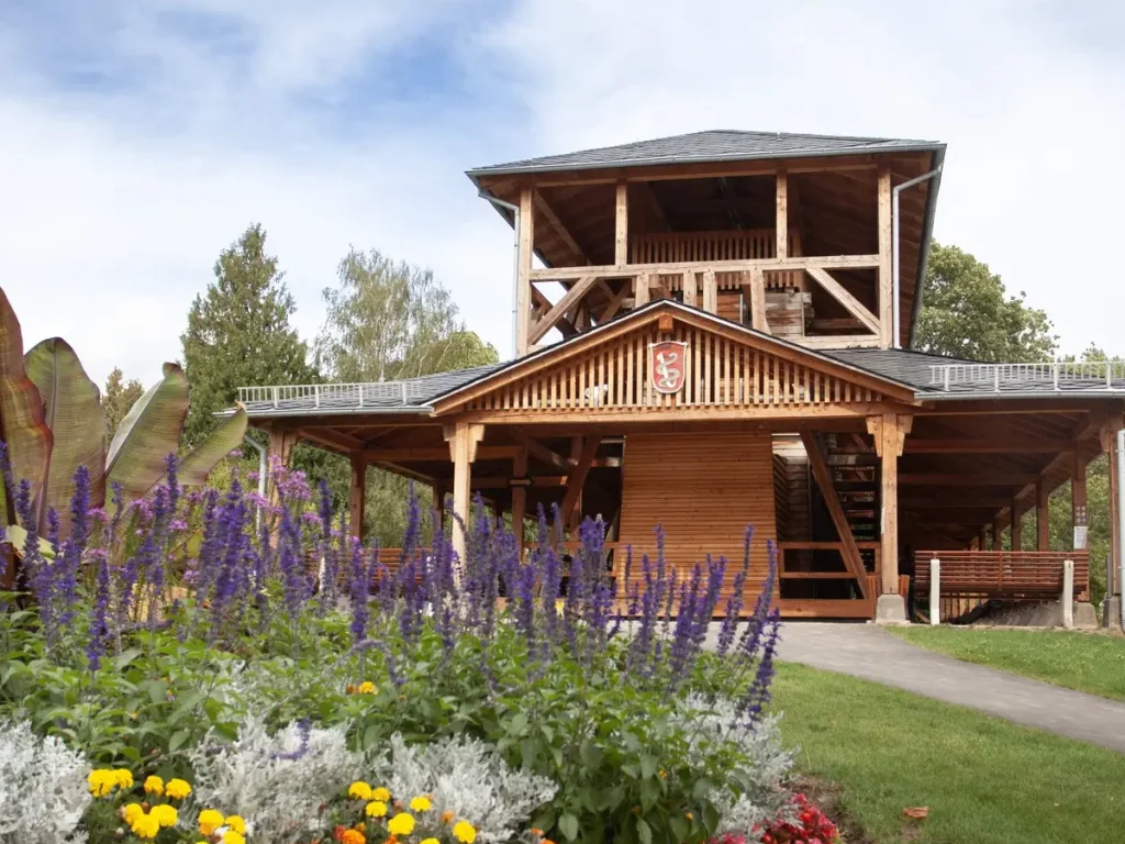 Historisches Gradierwerk im Kurpark Bad Salzhausen mit hölzerner Konstruktion und überdachtem Aussichtsturm. Im Vordergrund blühen violette Blumen.