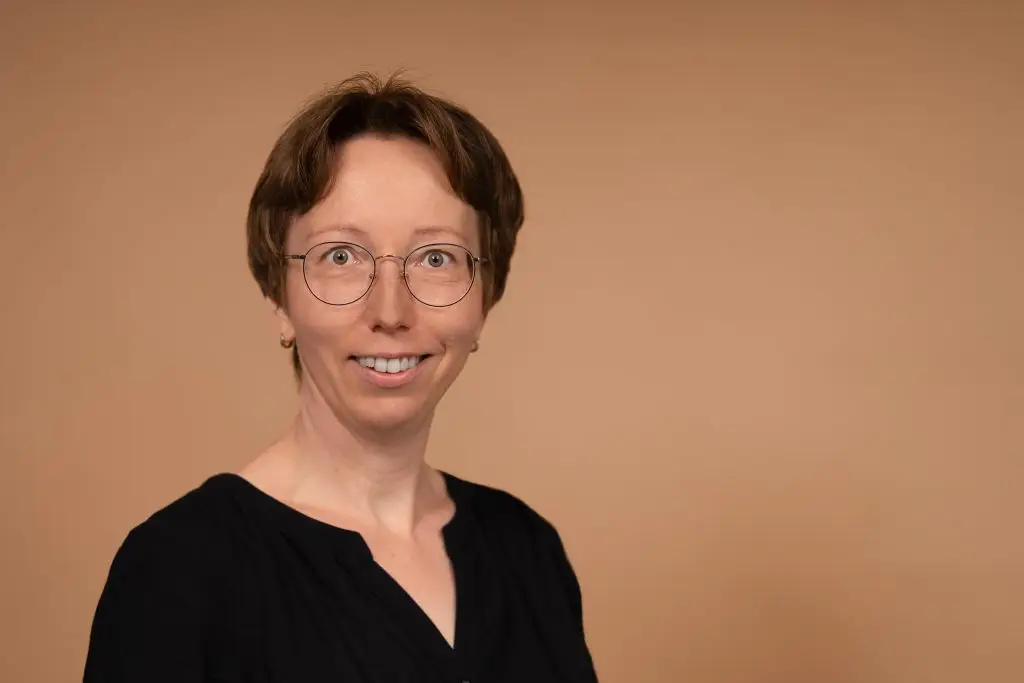 Porträt von Katrin Anja Krauße mit kurzer brauner Frisur, runder Brille und schwarzem Oberteil.