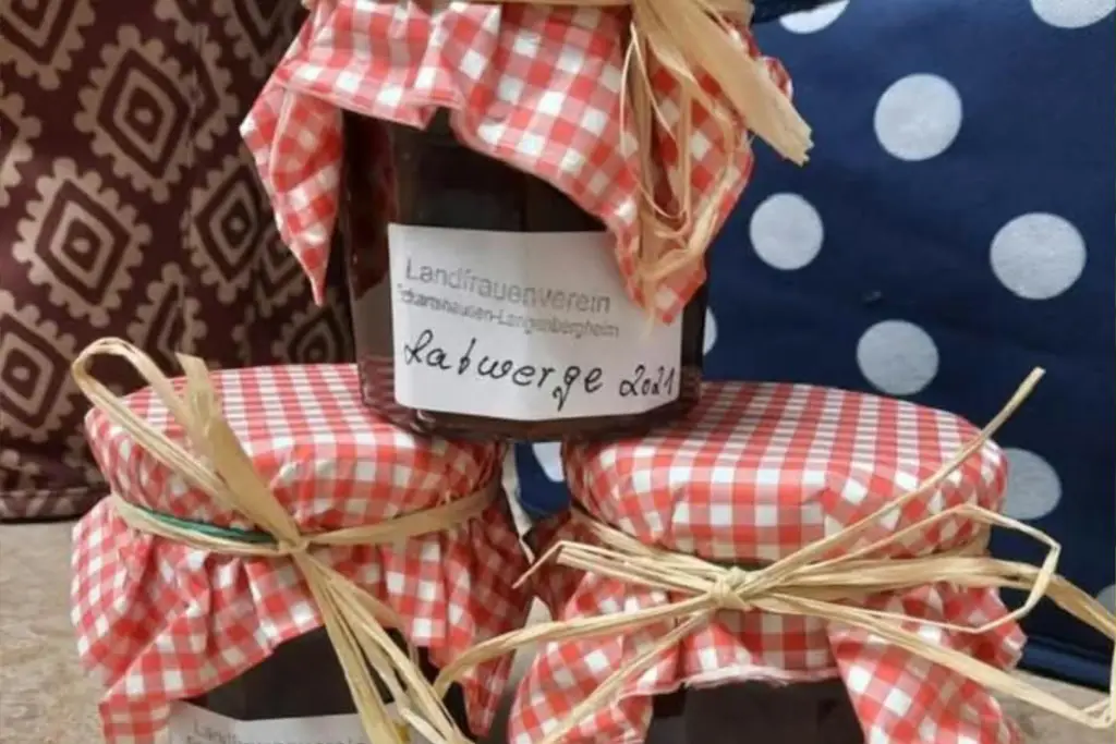 Drei dekorativ verpackte Marmeladengläser mit karierten Stoffhauben und Schleifen stehen auf einem Tisch.