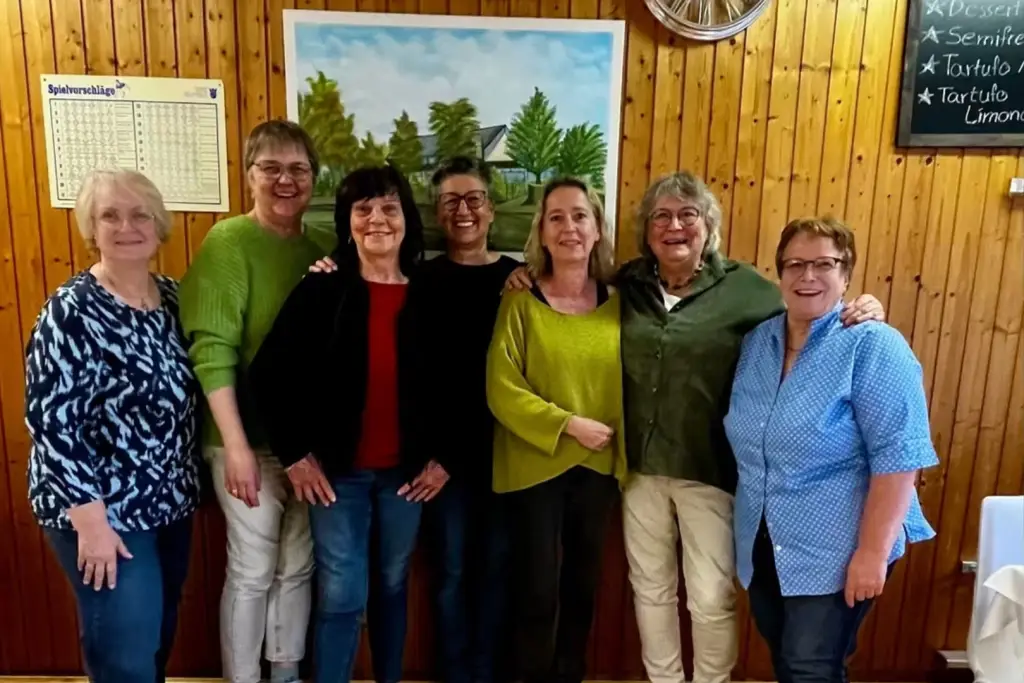 Sieben Personen stehen für ein Gruppenfoto vor einer holzverkleideten Wand in einem Veranstaltungsraum.