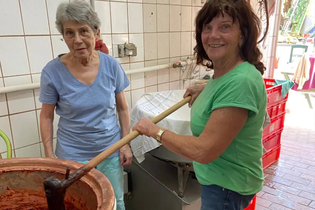 Zwei Personen rühren in einem großen Kupferkessel eine dunkle Fruchtmasse in einer Verarbeitungsküche.