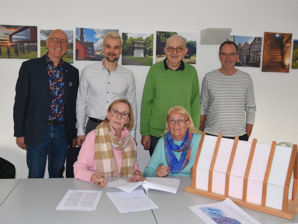 Sechs Personen bei der Unterzeichnung der Nutzungsvereinbarung für die Lichtkirche. Zwei Frauen sitzen an einem Tisch mit Dokumenten, vier Männer stehen dahinter.